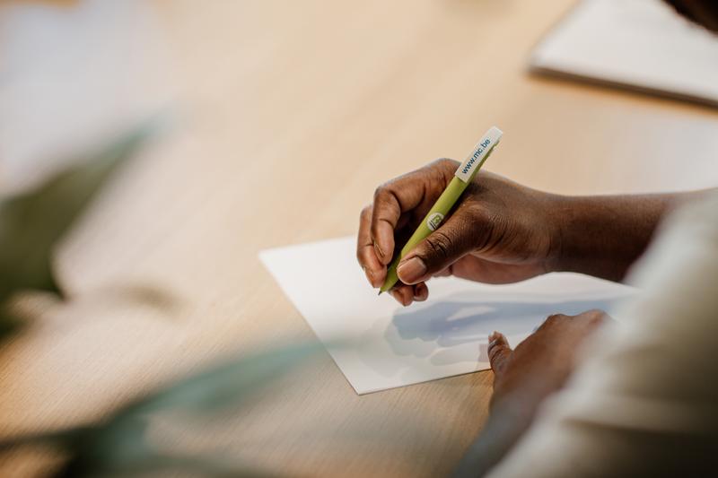 Iemand schrijft met een balpen met CM-opschrift