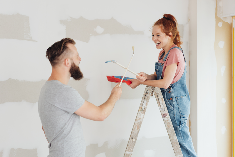 Laughing young couple fooling around with paintbrushes and a tray of paint during DIY renovations to their new home