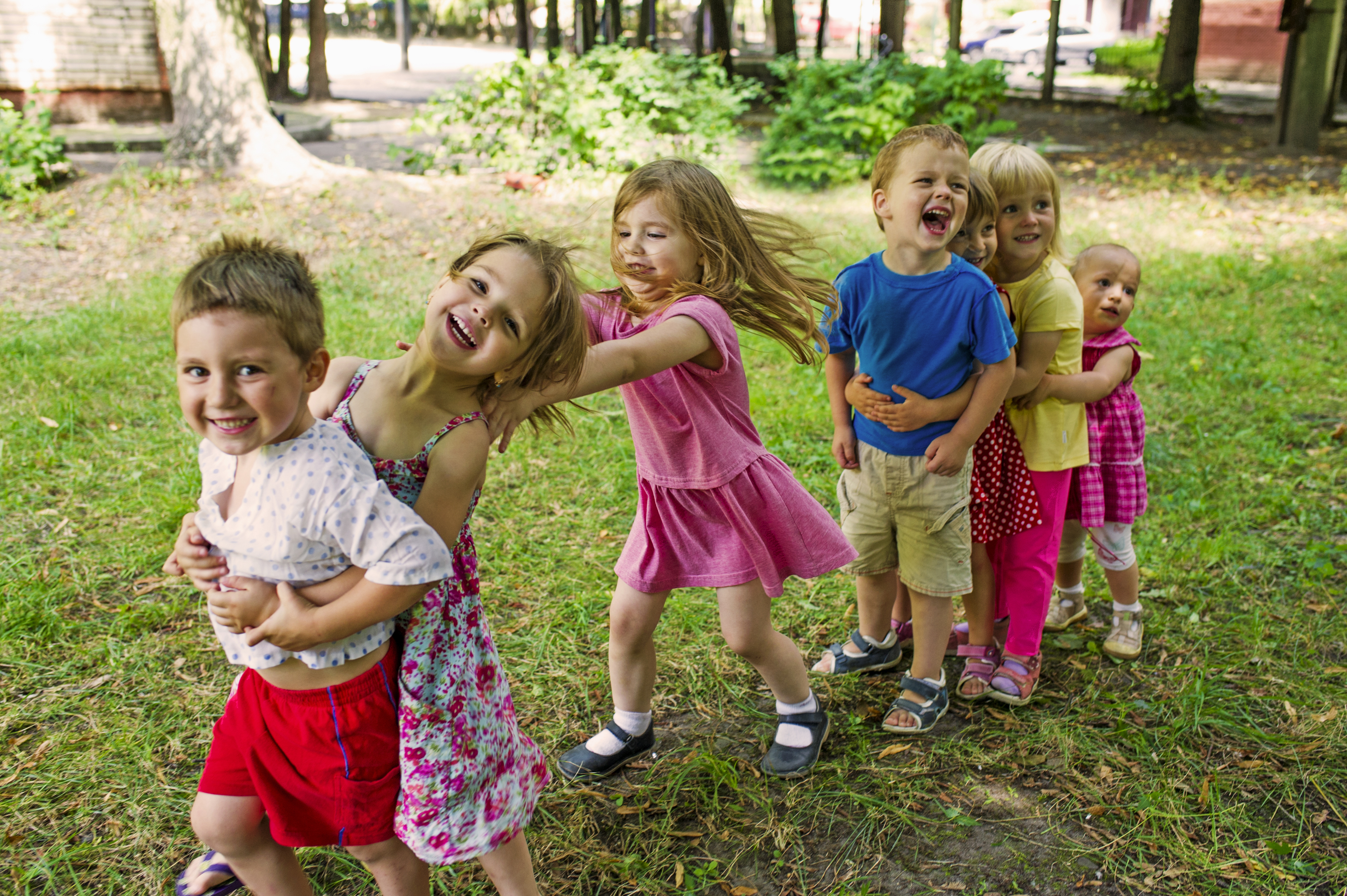 Kinderen lopen in een rijtje achter elkaar op een grasveld