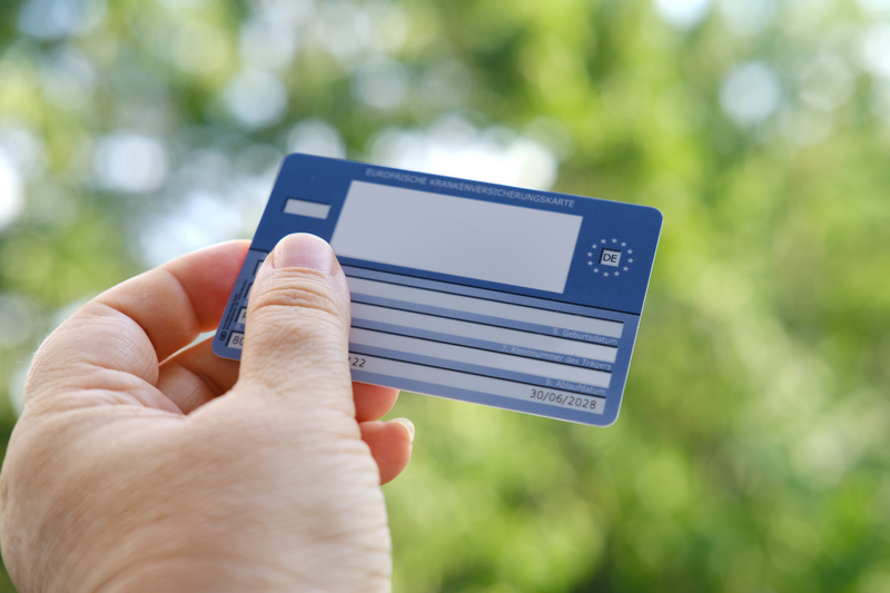 German health insurance card in female hand on natural green background, blue EU document healthcare support, medical expenses, emergency, Europeans Travel insurance traveling to EU and EFTA countries